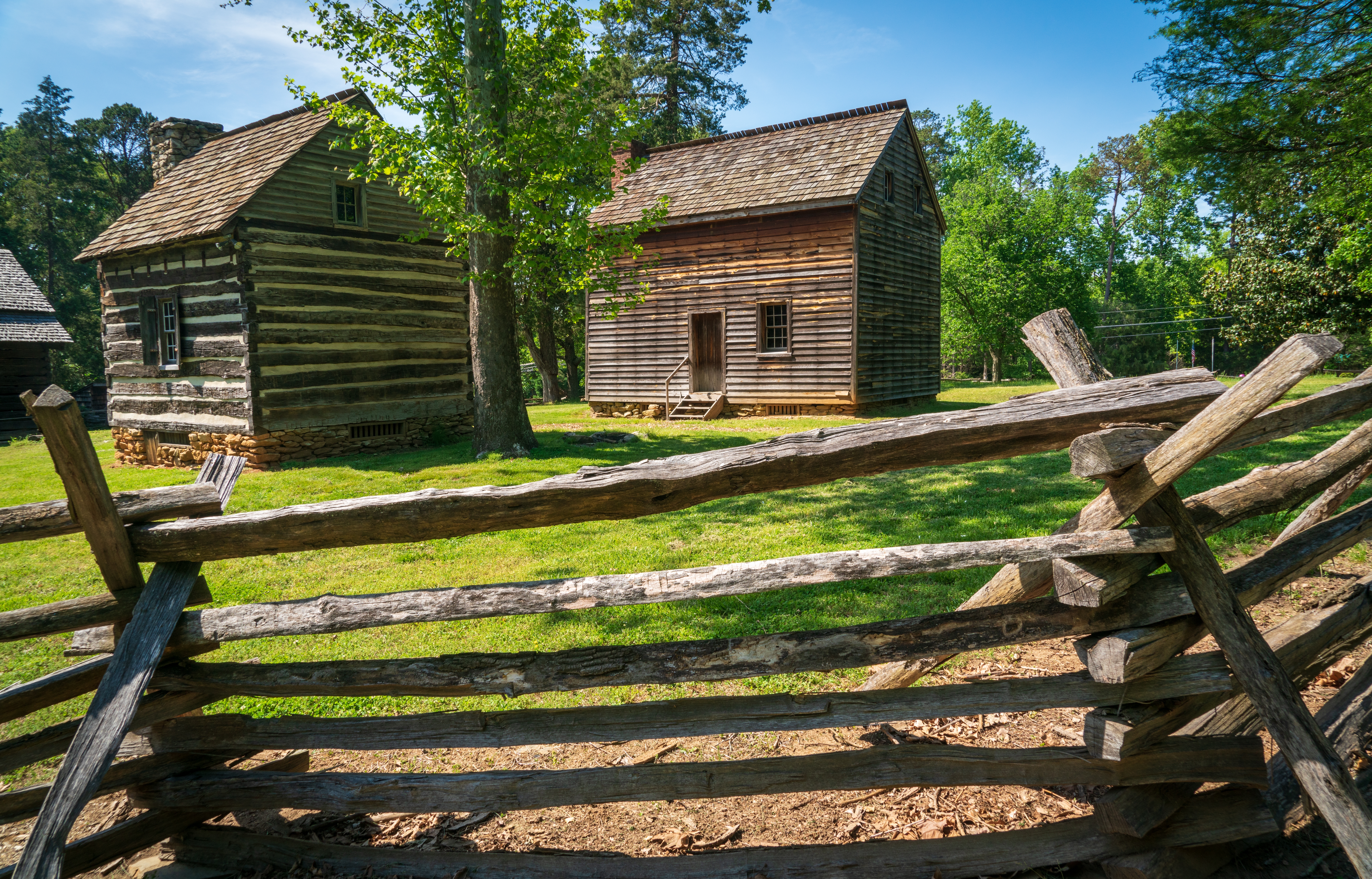 Restored 18th century cabins and a farmhouse in a grassy field at Guilford Courthouse National Military Park in Greensboro North Carolina