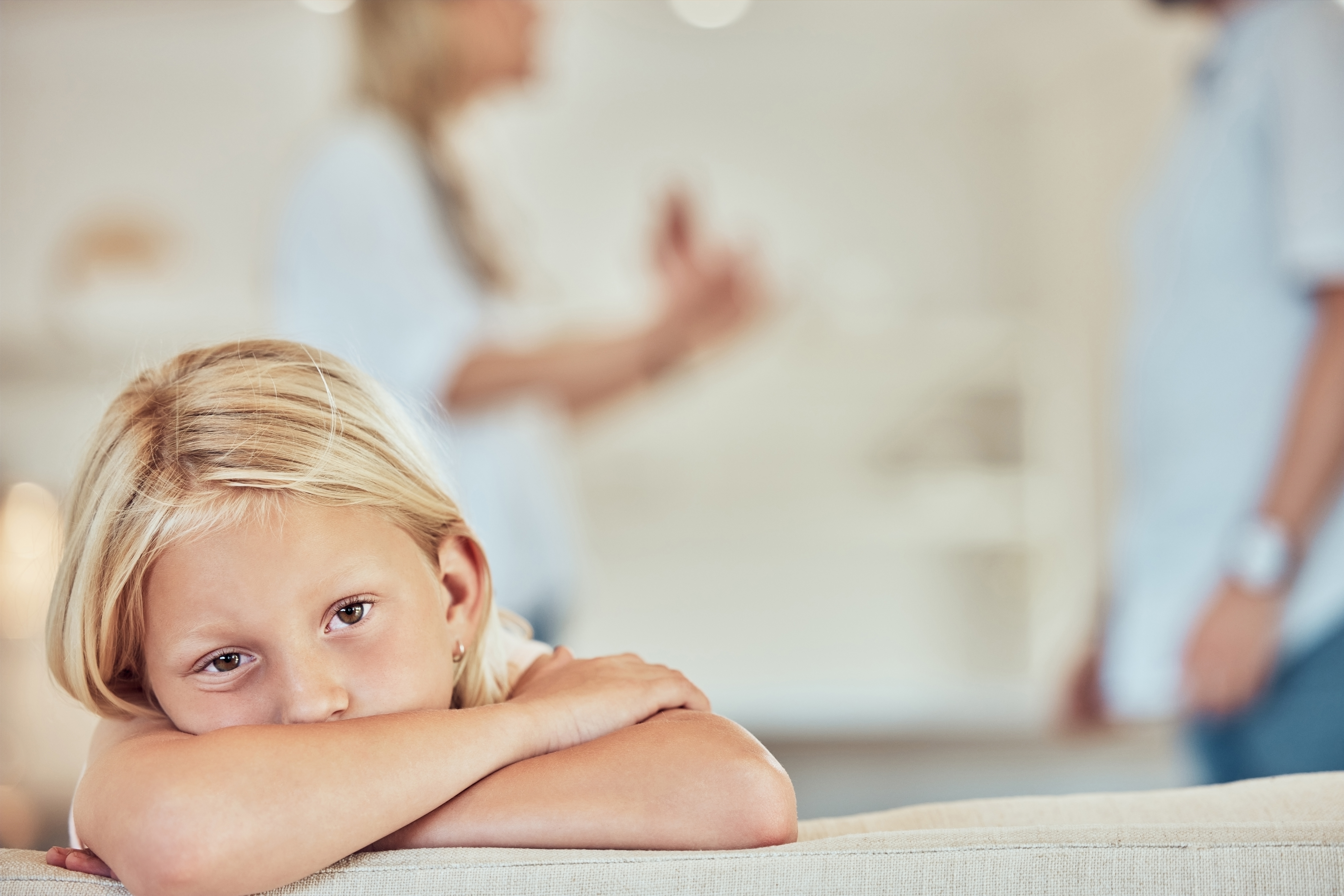 A sad young girl sits on a couch with her head down while her parents argue in the background about child custody in Huntersville, North Carolina.